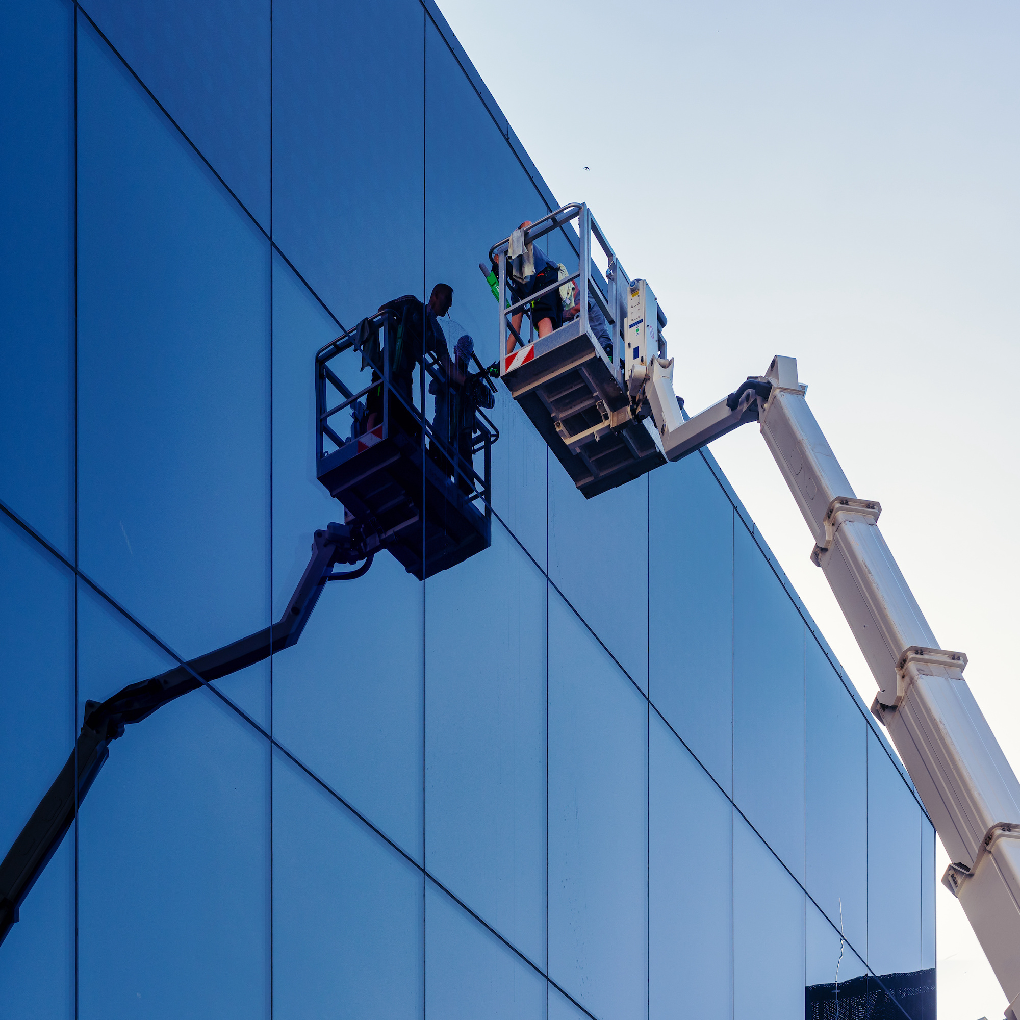 Cleaner worker using a cherry picker to clean a glas  facade of a contemporary office building.